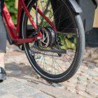 A closeup at a black kickstand on a red bike, you can see that a woman is walking with the bicycle