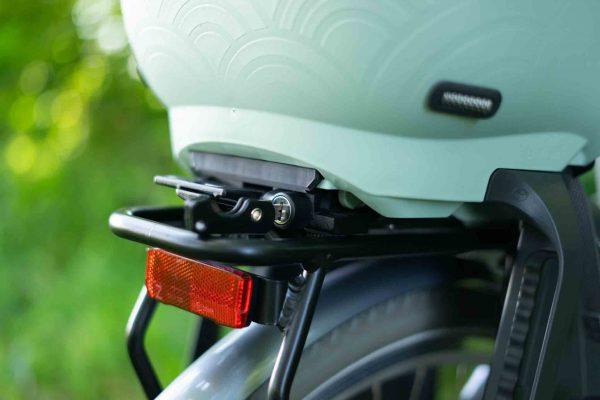 A closup on a rack on a trail with greenery all around. On top of it is a green childseat.