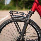 A front rack on a red bicycle, with asphalt and a forest visible in the background.