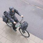 A woman biking in the rain with a front top bag, a top bag in the back and two side panniers. They are all wateproof and grey.