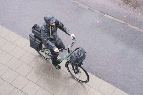 A woman biking in the rain with a front top bag, a top bag in the back and two side panniers. They are all wateproof and grey.