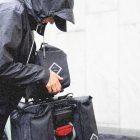 A woman lifting up a top bag from the rear carrier in the rain.