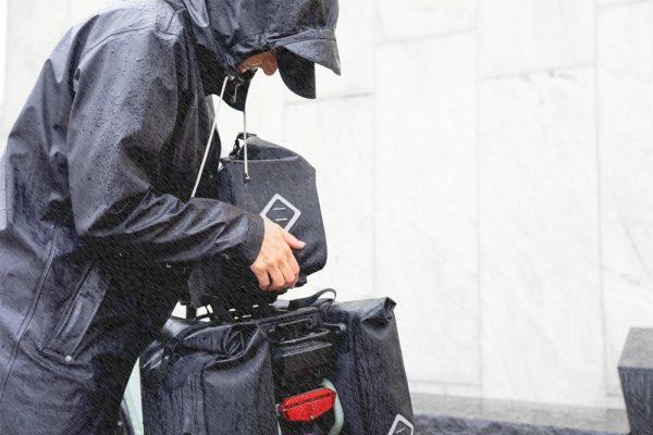 A woman lifting up a top bag from the rear carrier in the rain.