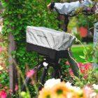 A basket in a garden with flowers, it has a reflective raincover.