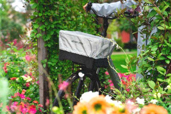 A basket in a garden with flowers, it has a reflective raincover.