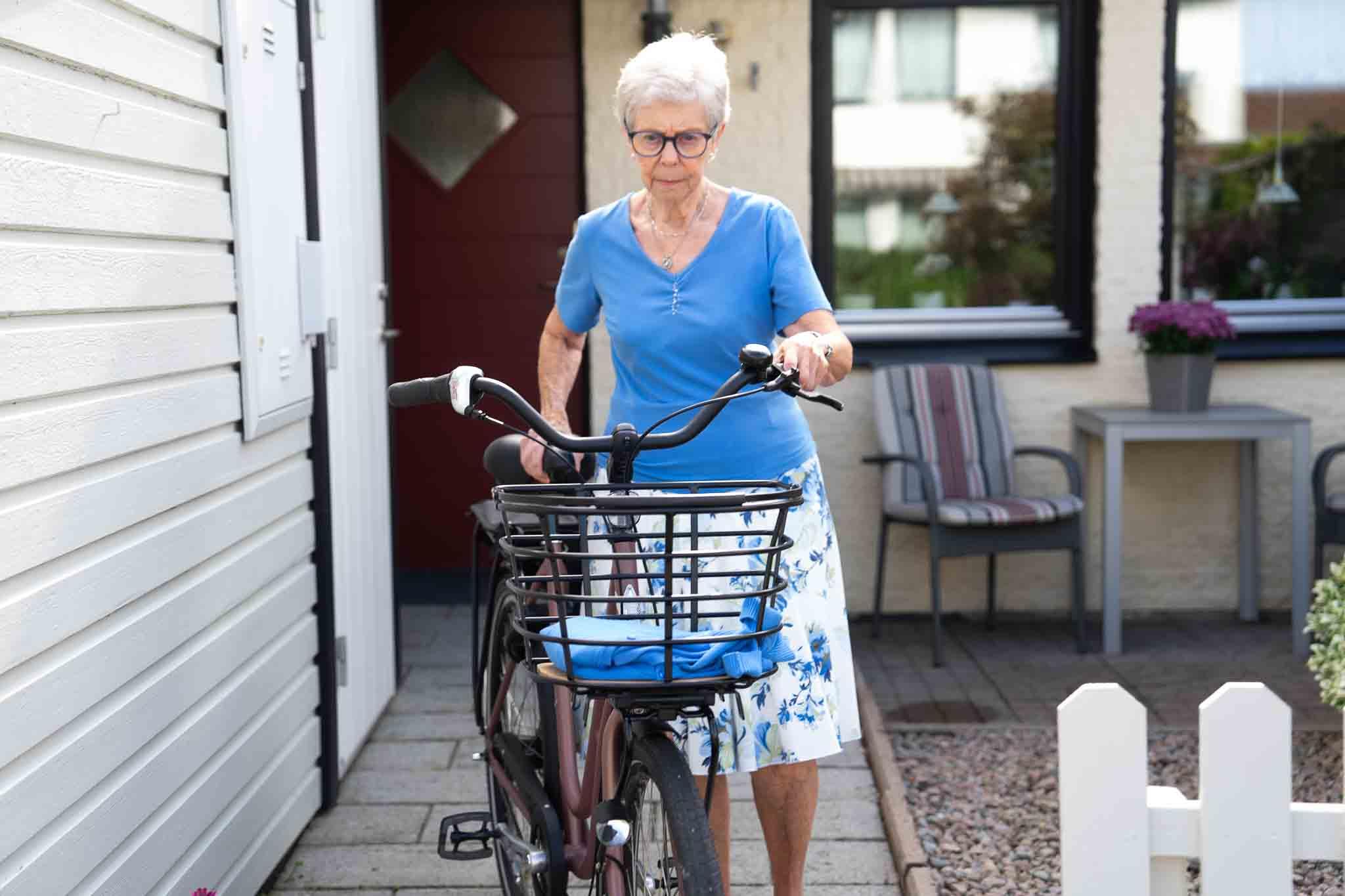 A lady walking from her home with a curved basket on her bicycle