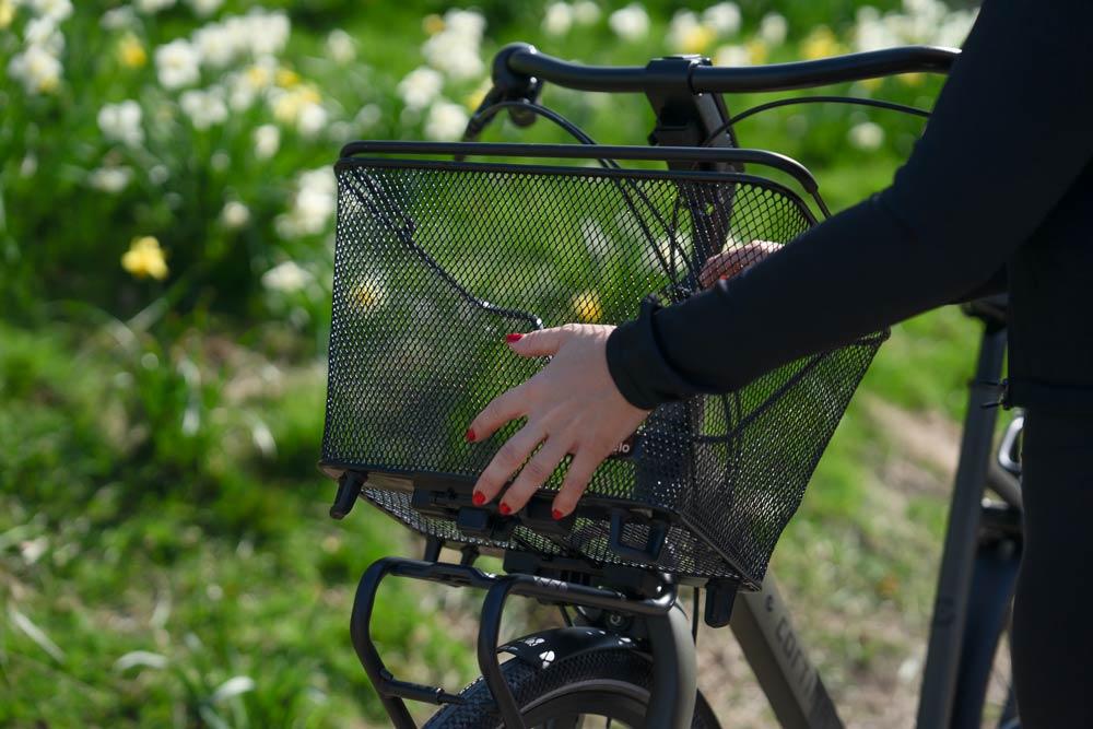 A girl taking off a mesh basket from a front carrier. In the background you can see grass.