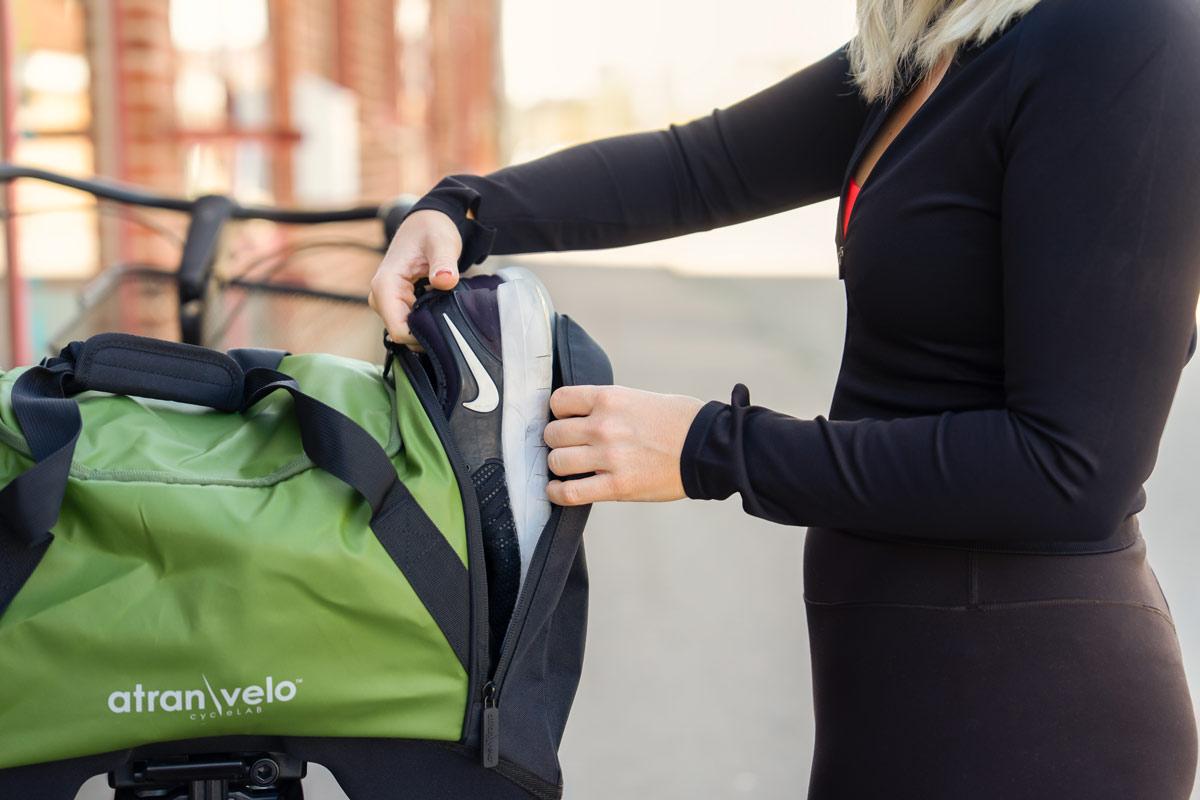 A girl dressed in black taking out shoes from a pocket from a green gymbag.