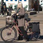 Girl biking through town with a basket in the front and two sidebags