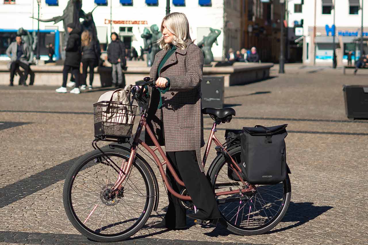 Girl biking through town with a basket in the front and two sidebags