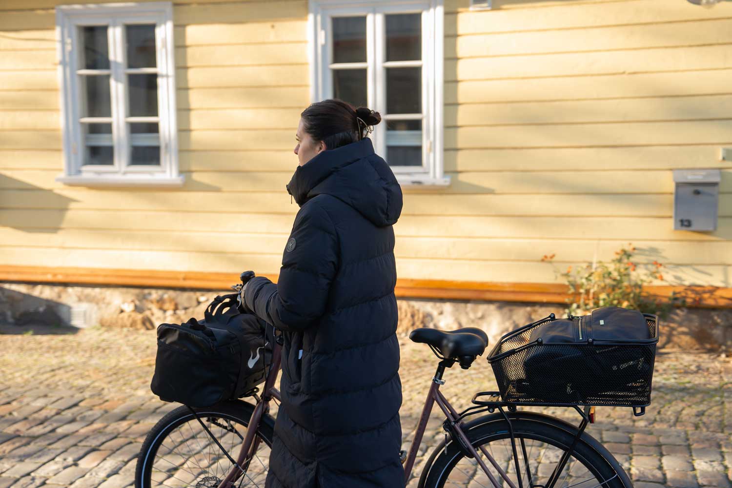 A woman walking with her bike with a basket in the back and a crate in the front