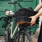 A girl lifiting up a black basket with an infill from her green bike. In the background there is a green door.