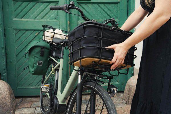 A girl lifiting up a black basket with an infill from her green bike. In the background there is a green door.