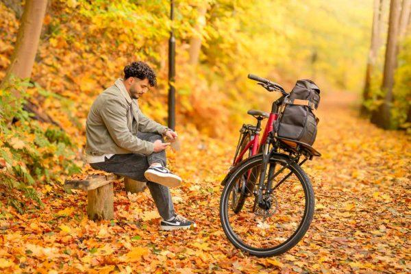 A man sitting on a bench in a yellow autumn forest with his bicycle infront of him