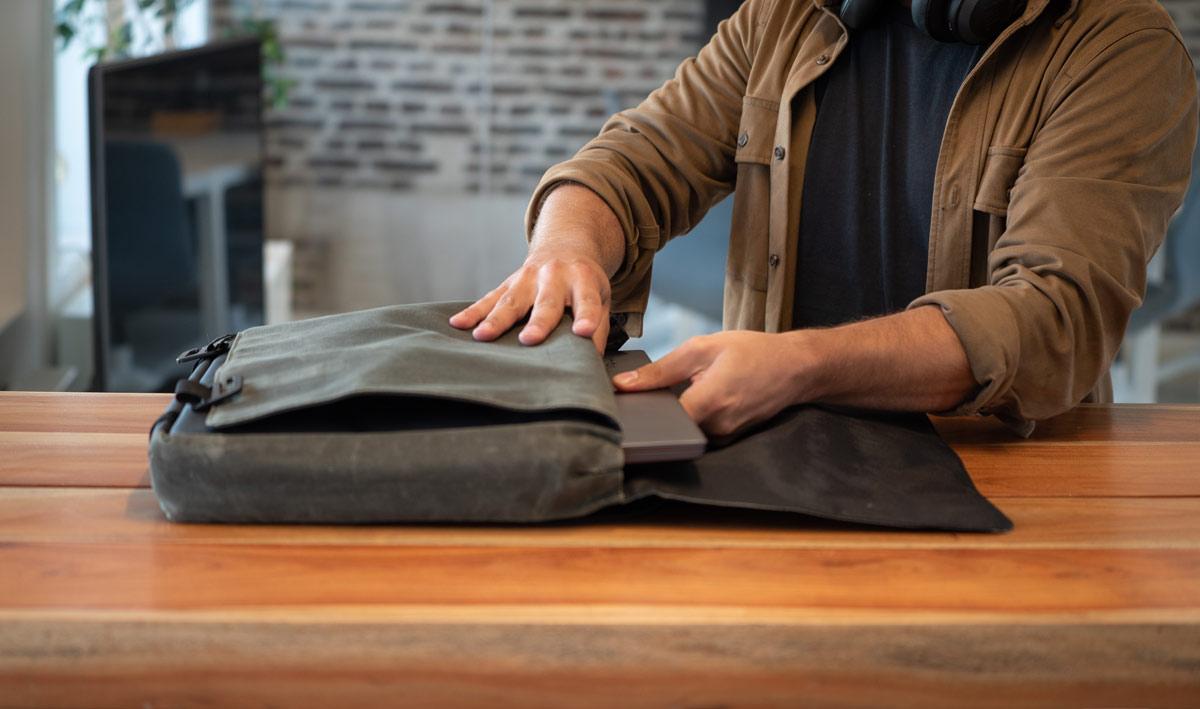 A man sitting at a table in a cafe putting in his computer in his bag