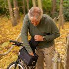 A man looking inside a front top bag on a bicycle in a yellow autumn forest.