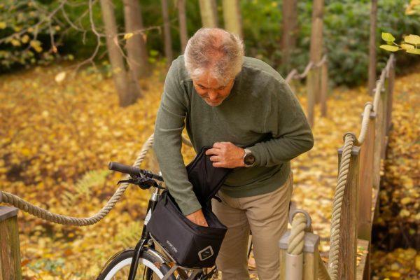 A man looking inside a front top bag on a bicycle in a yellow autumn forest.