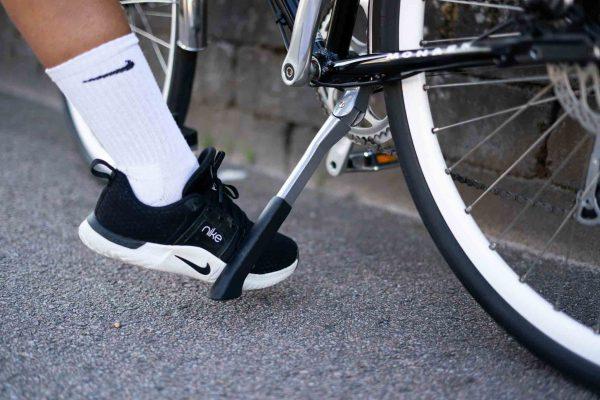 Close-up of a foot lifting up a chrome-colored bike stand.