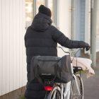 A woman walking in the winter with a bicycle. On the rear carrier she has a big sporty bag.
