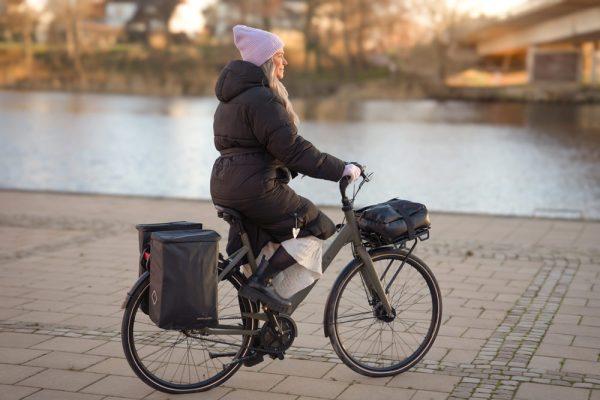 A girl biking by a river with two bags on the rear carrier