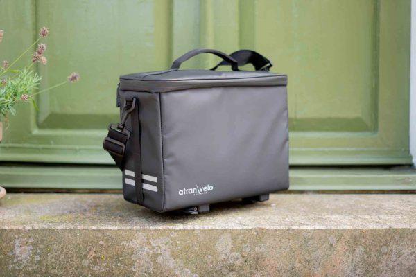 A grey topbag on a stair with a green door in the background