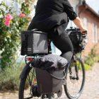 Woman on a bike from ehind in an old charmy town, on the bike there is a crate and a topbag