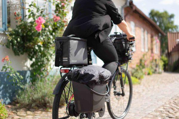 Woman on a bike from ehind in an old charmy town, on the bike there is a crate and a topbag