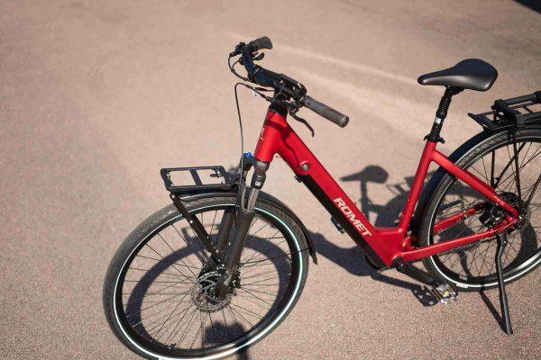 A front rack on a red bicycle, with asphalt and a forest visible in the background.