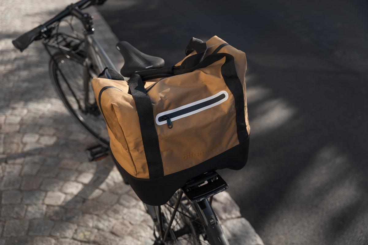 A bicycle from the back outside with a brown top bag on the rear carrier
