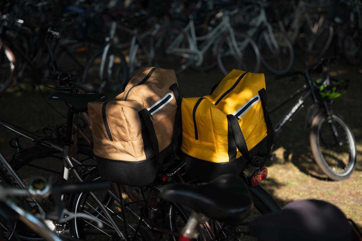 Two bicycles standing next to each other, one with a yellow top bag and one with a brown top bag.