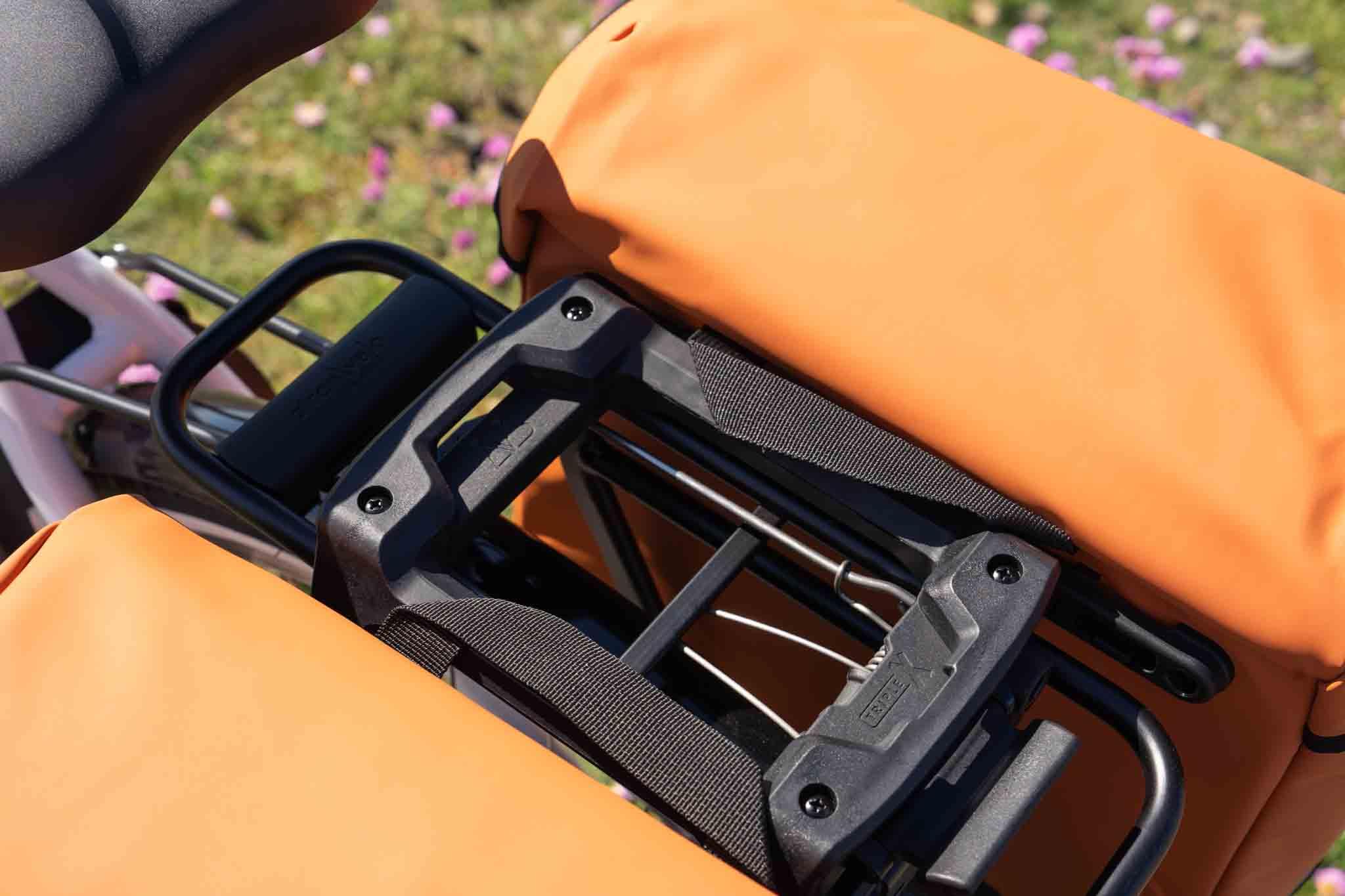 The triple-x system with two orange bags hanging on the sides of a bicycle, close-up.