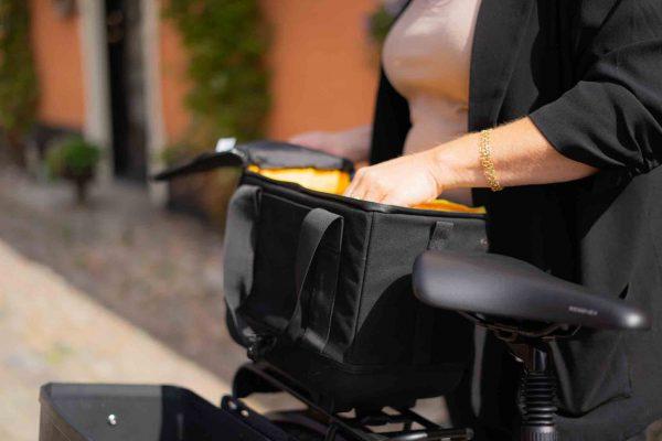 A black top bag with a yellow interior on a bicycle, with a woman's hand rummaging inside the bag.