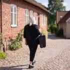 A woman walking from behind on a charming old cobblestone street, with a side basket around her arm.