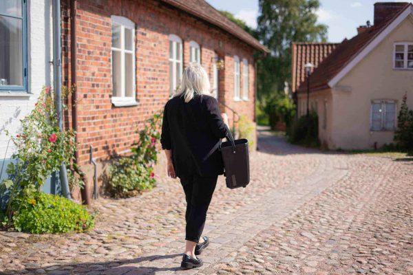 A woman walking from behind on a charming old cobblestone street, with a side basket around her arm.