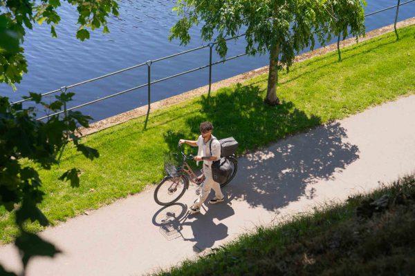 A guy walking with a bicycle that has three gray bags on it.