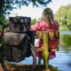 Woman on a bench by a lake, a bike with three bags in focus