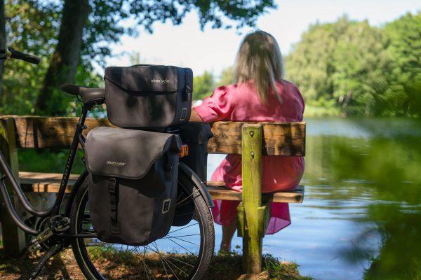Woman on a bench by a lake, a bike with three bags in focus