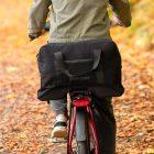 A closeup at a big black top back on a rear carrier, a man is biking.