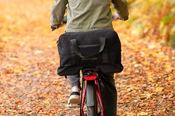 A closeup at a big black top back on a rear carrier, a man is biking.