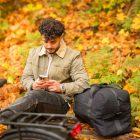 A man sitting on a bench in a yellow forest, he has his elbow on a big bicyclebag. In the front of the picture you see a blurred carrier.