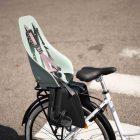 A white bicycle with a black rack at a crosswalk with a childseat on top.