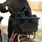 A girl with a black basket in the front of a bike .in the background you can see a river.