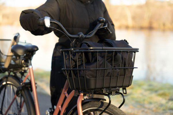 A girl with a black basket in the front of a bike .in the background you can see a river.