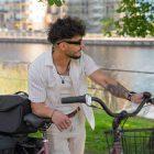 A man is leaning against a bicycle, and there is a gray top bag on the bike.