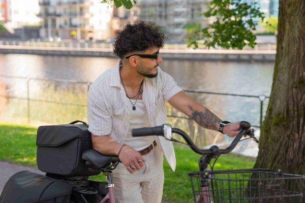 A man is leaning against a bicycle, and there is a gray top bag on the bike.