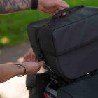 A male hand with rings lifting a top bag onto a bicycle.