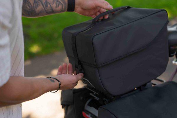 A male hand with rings lifting a top bag onto a bicycle.