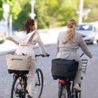 Two women biking from behind with one stylish and feminine bag each, one in black and one in beige.