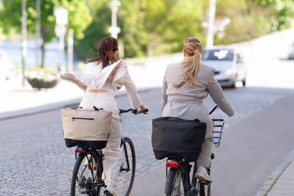 Two women biking from behind with one stylish and feminine bag each, one in black and one in beige.