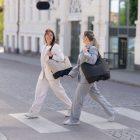 Two business women walking across a crossing with one stylish and feminine bag each. One in black and one in beige.